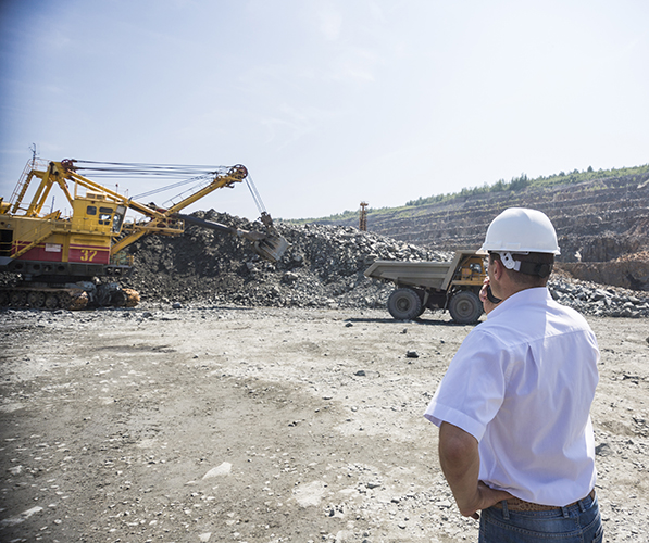 Mining engineer in white shirt and helmet supervises loading dumpers in quarry